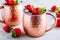 Refreshing iced Moscow mule alcoholic cocktail in copper mugs with strawberry and lemon