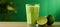 Refreshing lime juice in glass on wooden table with soft green background for text placement