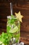 Refreshing mojito beverage with fresh lime, mint twigs, crushed ice, decorative carambola and sugar on a dark wooden background.