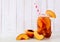 Refreshing peach iced tea in a mason jar glass with cut fruit against white wood