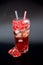 Refreshing pomegranate juice with ice and seeds in a tall glass on a black background, next to a broken fruit
