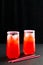 Refreshing summer mocktails with ice cubes. Two tall glasses of iced red juice with straws on dark background.