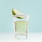 Refreshing tequila drink with slice lime, salt in shot glass on soft light white wood board and pastel green interior, square.