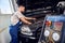 Refueling the air conditioner. A mechanic pumps freon into the air conditioning system at a car service