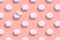 Regular pattern of closed jars of cream on a pastel pink background. Minimal skin care concept