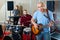 Rehearsal of music group. Band leader playing guitar and singing with his musicians in recording studio