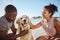 Relax, couple and dog at a beach, happy and smile while bonding, sitting and touching their puppy against blue sky