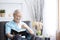 Relax elderly man sitting on sofa and reading interesting book in living room