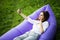 Relax on fresh air. Pretty young woman lying on inflatable sofa lamzac use mobile phone while resting on grass in park on the sun