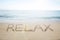 Relax word handwritten in sand on sunny beach
