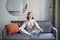 Relaxation and patience. Smiling young asian woman in cozy room, sitting on sofa and meditating, doing yoga mindfulness