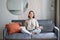 Relaxation and patience. Smiling young asian woman in cozy room, sitting on sofa and meditating, doing yoga mindfulness