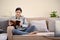 Relaxed Asian female sitting on her sofa in a minimalist living room, casually reading a book