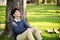 Relaxed Asian man sitting under the tree, eyes closed, chilling at the beautiful greenery park