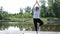 A relaxed athletic mature woman does yoga in the park, near the lake. A woman on a yoga mat to relax outdoors. An