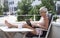 Relaxed barefoot senior woman sitting and typing on a laptop computer outside on a balcony