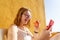 Relaxed blond teen laughing while eating a red apple, lying in the terrace of the resort and making a video call in her smart