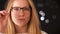 Relaxed blonde caucasian girl in glasses with smart look , touching her glasses confidently while looking at camera with