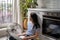 Relaxed carefree Asian woman sits on floor with laptop on lap and enjoying wind coming from fan