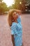 Relaxed and carefree woman who tilts her head to the left, touches her long hair, stands in the park