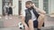 Relaxed Caucasian schoolboy in Covid face mask sitting on school stairs with sport ball and listening to music in