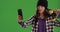 Relaxed Chinese skater girl using smart phone to take selfie on greenscreen