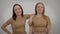 Relaxed confident twin sisters posing at grey background looking at camera laughing. Portrait of two positive Caucasian