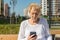 Relaxed elder woman sitting on a bench with smartphone. Happy old age concept