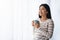 Relaxed Korean Female Drinking Coffee While Standing Near Window At Home