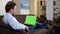 Relaxed male on couch using green screen laptop shopping online, booking service