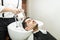 Relaxed Man Leaning On Sink While Hairdresser Washing His Hair