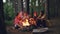 Relaxed men and women travelers are singing songs around campfire in forest, playing the guitar and roasting marshmallow