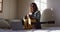 Relaxed mixed race woman in headphones sitting with guitar using laptop in sunny cottage bedroom