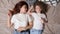 Relaxed mother and preschooler daughter lie on grey bed