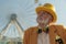 Relaxed old man in ridiculous hat near ferris wheel