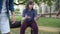 Relaxed plump boy sitting on bench with sandwich as unrecognizable aggressive classmates knocking out meal from his