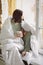 Relaxed positive young brunette woman in homewear sitting on top of unmade bed with cup of tea in her hands