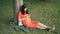 Relaxed pregnant girl is using smartphone touching screen sitting on grass in park on warm summer day. Pregnancy, modern