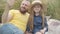 Relaxed pretty little girl in straw hat sitting on meadow with bearded man talking. Portrait of carefree beautiful