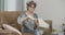 Relaxed senior woman in eyeglasses and curlers applying hand moisturizer sitting on couch at home in the evening