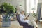 Relaxed senior woman sitting in armchair at home and reading book on digital tablet