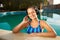 Relaxed smiling woman listening to music in headphones bathing in swimming pool. Blonde girl enjoys favourite song with