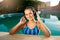 Relaxed smiling woman listening to music in headphones bathing in swimming pool. Blonde girl enjoys favourite song with