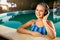 Relaxed smiling woman listening to music in headphones bathing in swimming pool. Blonde girl enjoys favourite song with