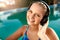 Relaxed smiling woman listening to music in headphones bathing in swimming pool. Blonde girl enjoys favourite song with