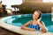 Relaxed smiling woman listening to music in headphones bathing in swimming pool. Blonde girl enjoys favourite song with