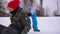 Relaxed teen boy sitting on green sled as girl pushing friend leaving. Portrait of joyful Caucasian friends having fun