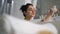 Relaxed woman cleaning body with foam in bathtub. Sexy girl washing skin in bath