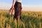 Relaxed woman legs walking in the middle of a field in summer holding shoes in hand.