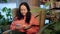 Relaxed woman using mobile phone in soft chair in indoor garden. Adult woman looking smartphone in cozy chair in flowers